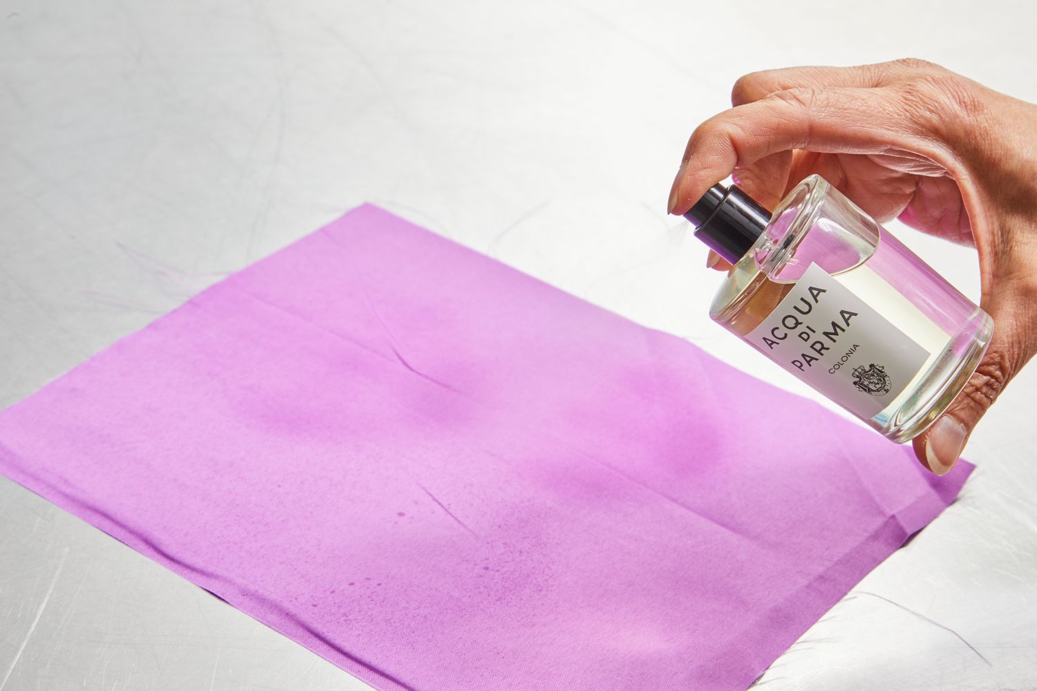 A hand spraying Acqua di Parma Colonia on a sheet